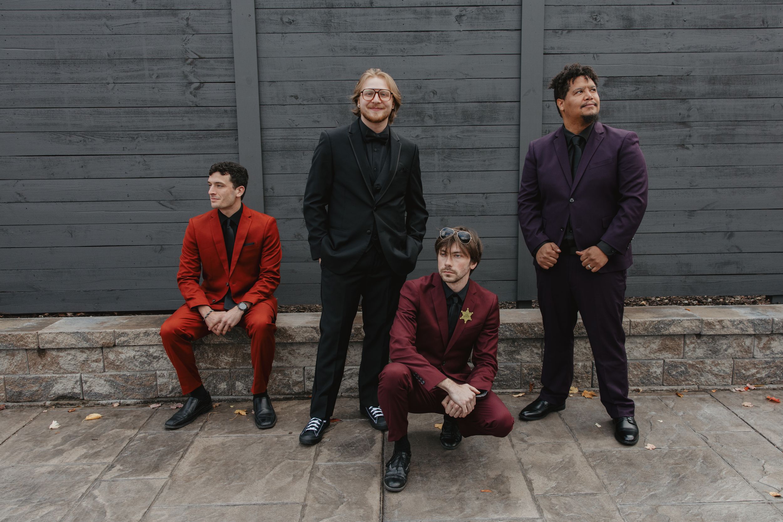 Four people in coordinated outfits sit casually against a gray wall for a stylized group photo shoot.