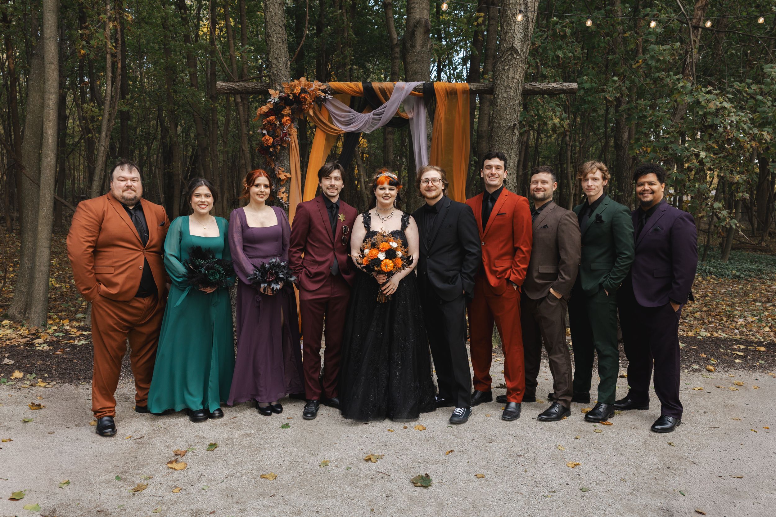 A group of people in fall attire stand together outdoors for a photo session in an autumn woodland setting.
