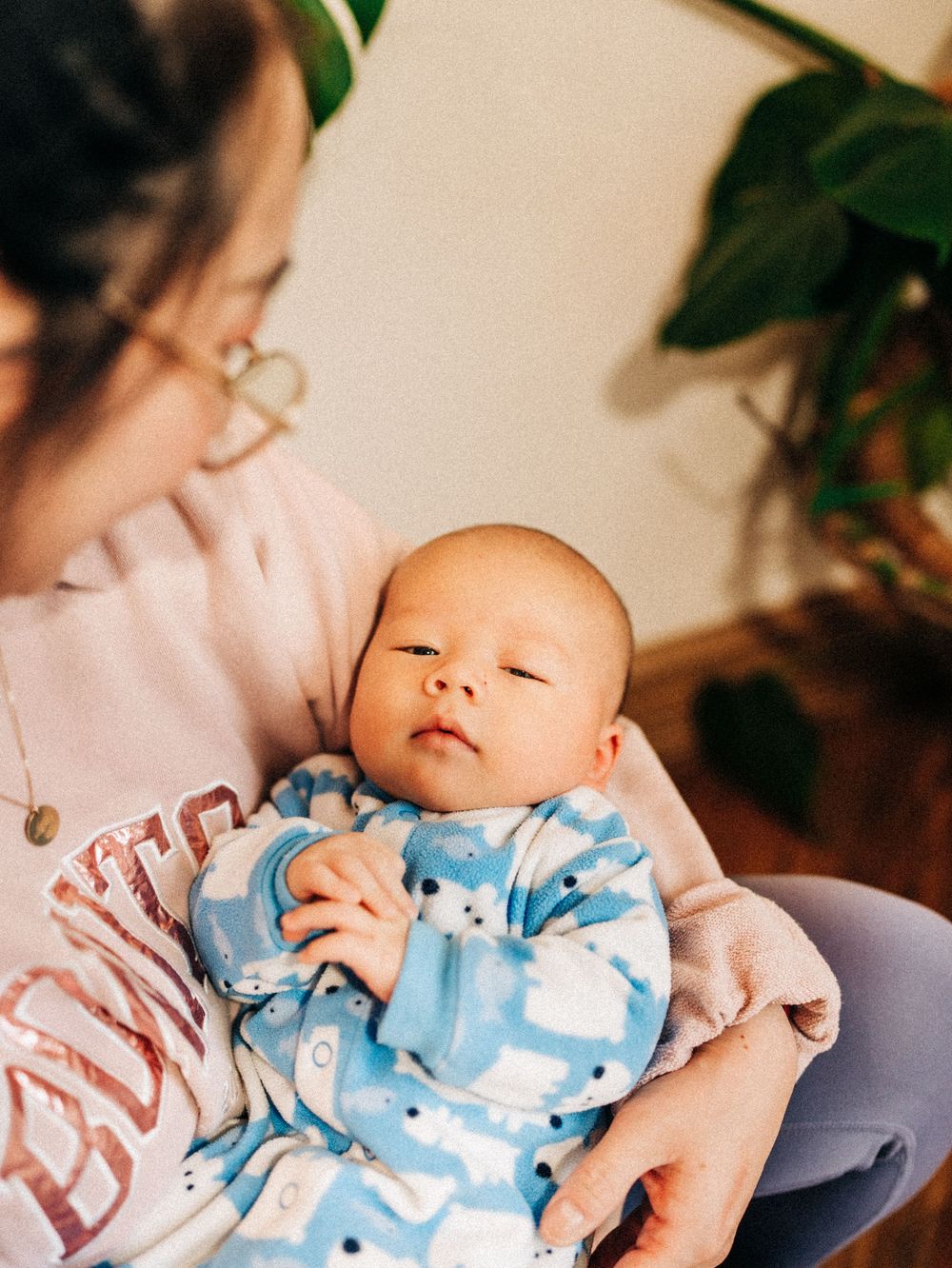 A sleeping baby in a blue patterned onesie rests peacefully while being cradled.