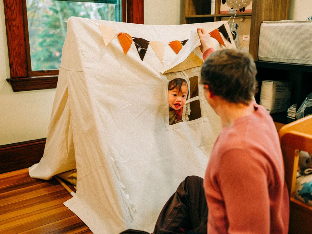 A white tent-like structure creates a fort in a living room with wooden floors and natural light coming through windows.