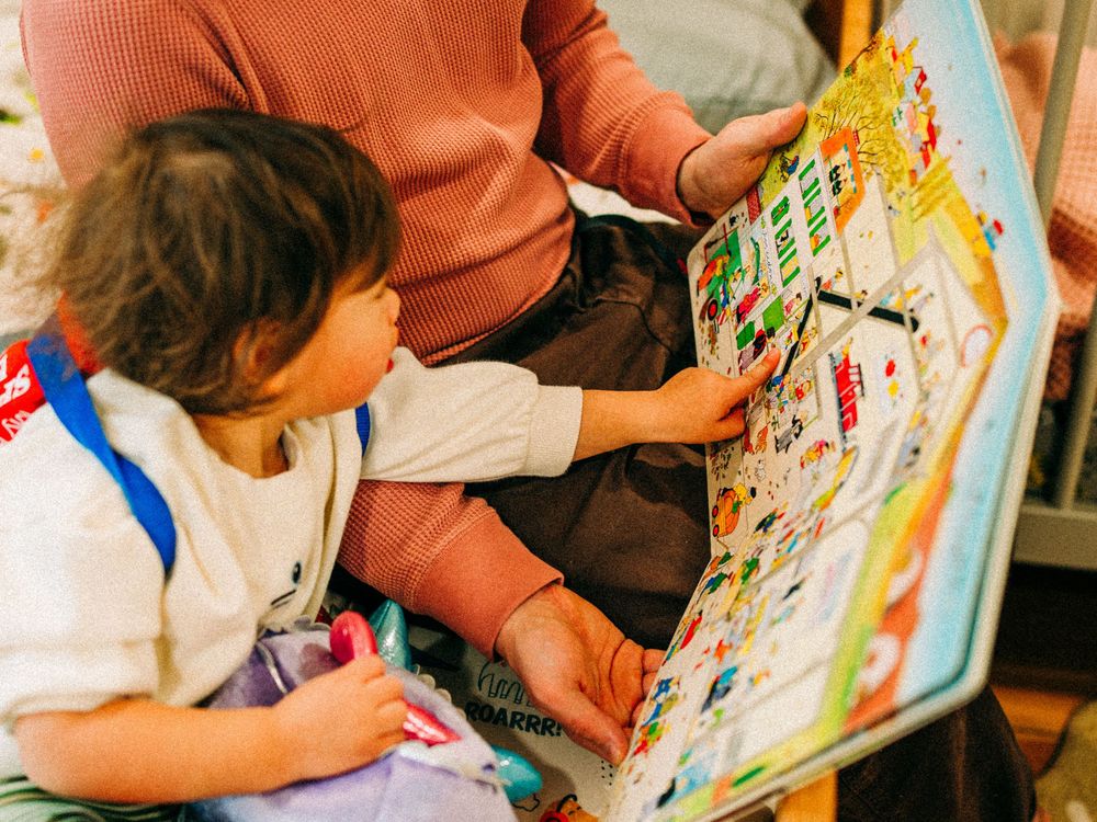 A person wearing an orange shirt sits at a table and draws in a colorful activity book with markers and art supplies.