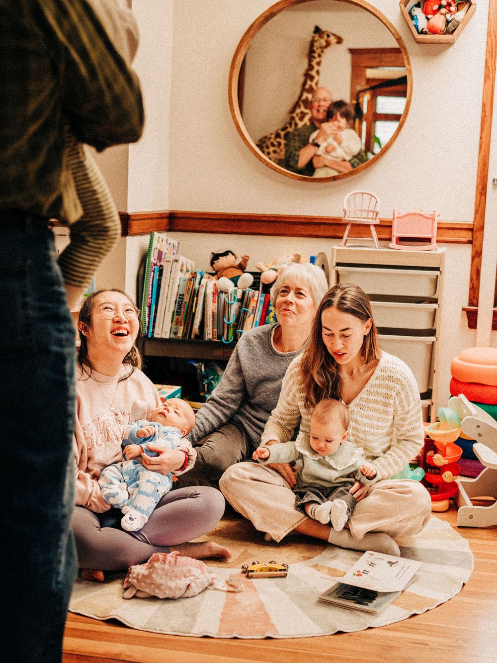 Family members sit together on a cozy floor blanket while reading books and sharing joyful moments together.