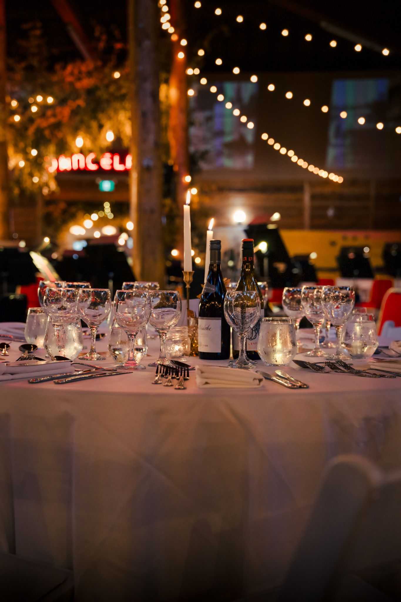 Elegant table settings with wine glasses line a long banquet table under twinkling lights.