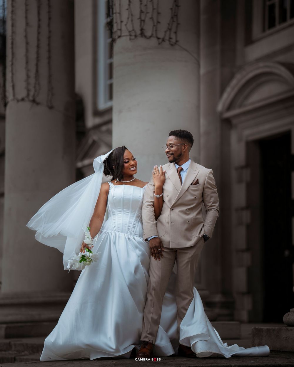 A joyful couple shares a candid moment together on their wedding day, with ornate architectural columns in the background.
