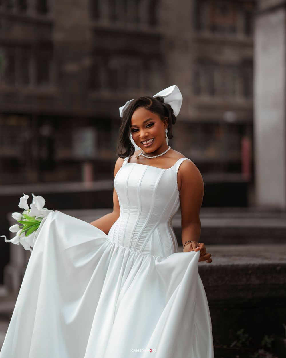 A person in a flowing white dress twirls and poses gracefully in an urban setting.