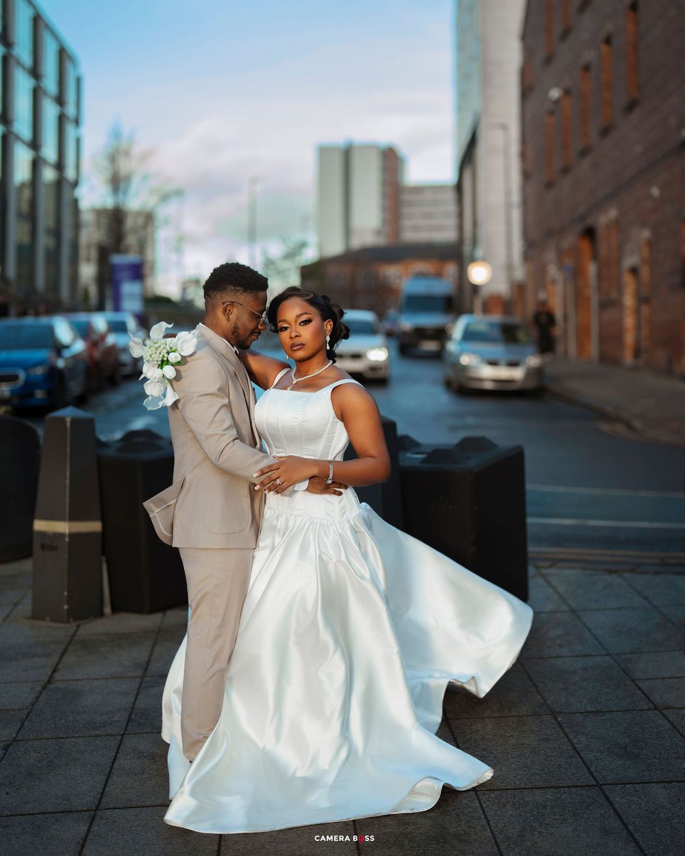 A couple dances together outdoors, with the bride's white dress flowing elegantly against an urban backdrop.