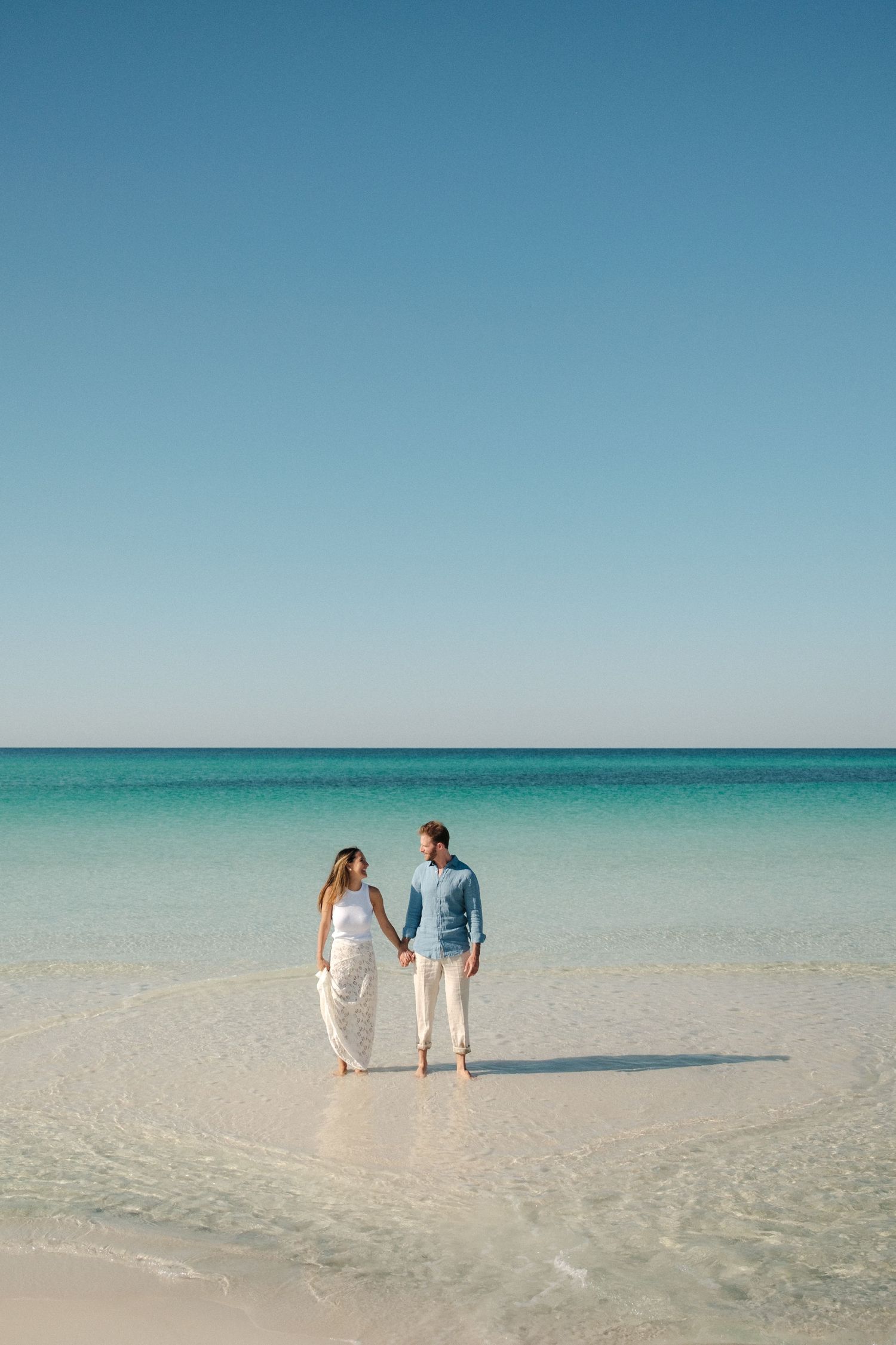 A couple in matching white outfits holding hands on a sunny day.