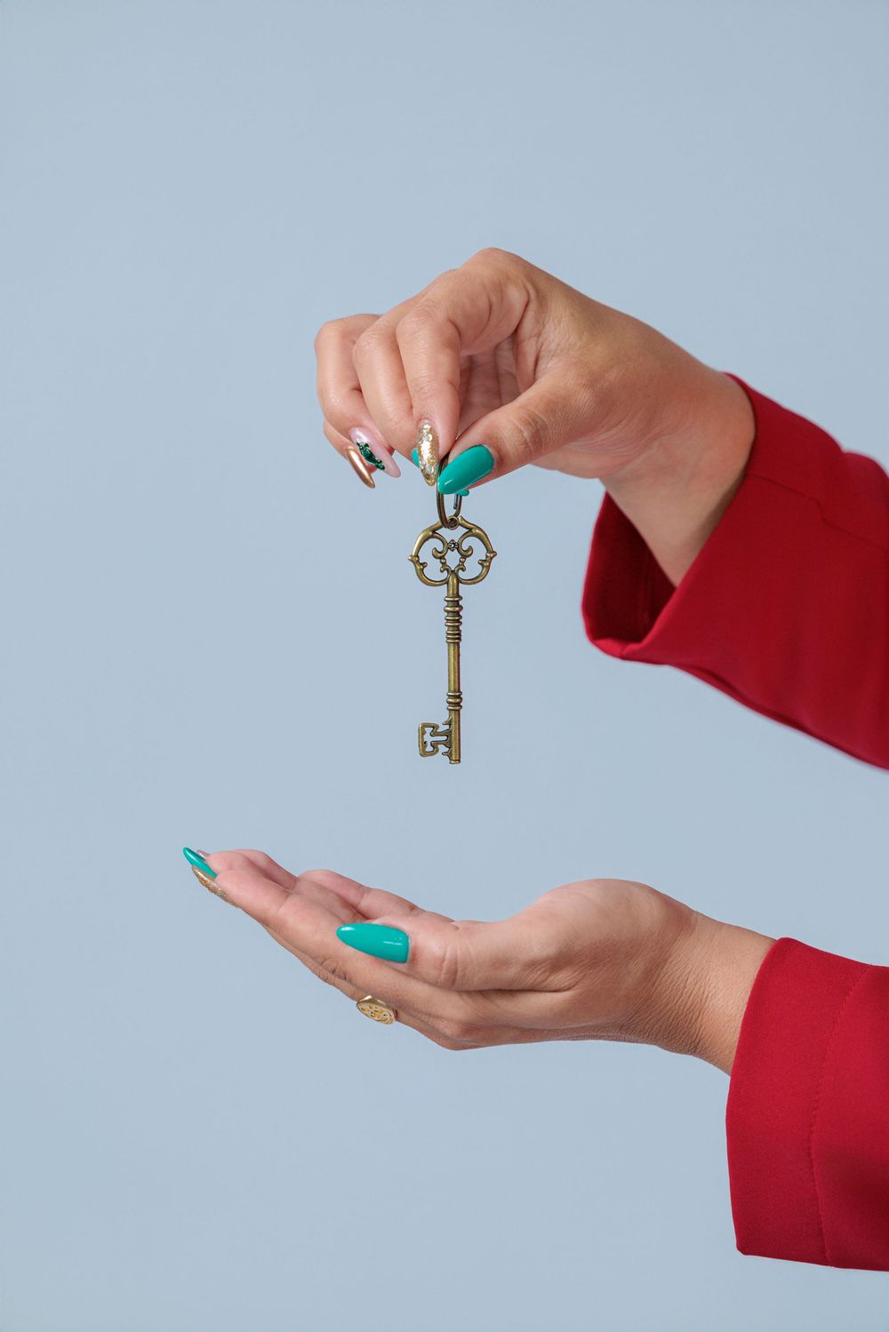 Female hands with teal nail polish holding ornate vintage gold key against light blue background.