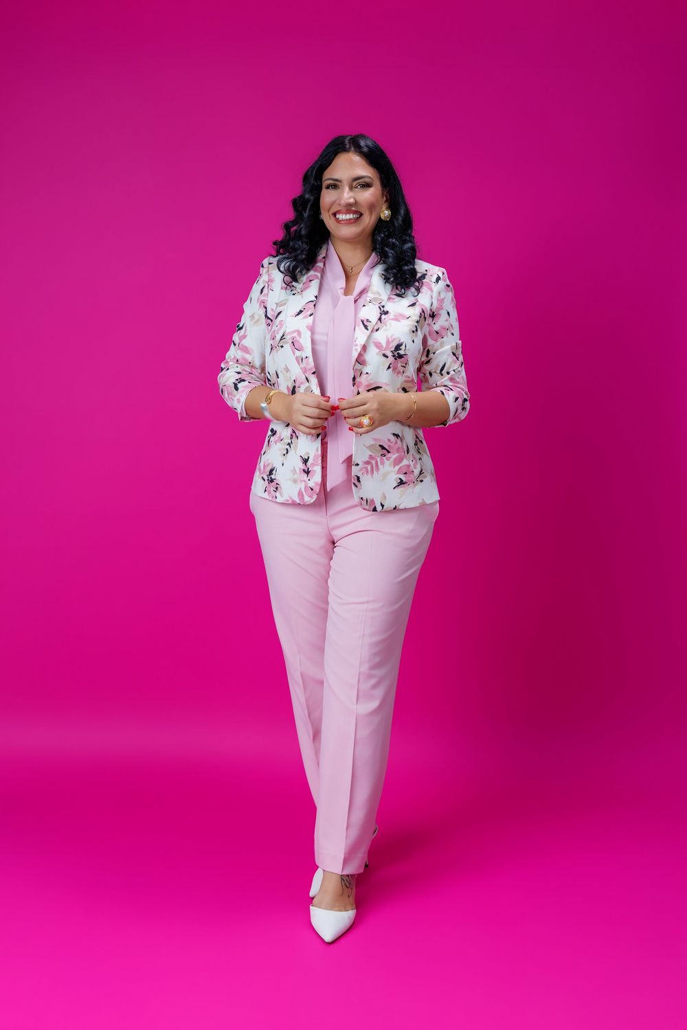 Woman in floral blazer and pink pants smiling confidently against a vibrant magenta background.