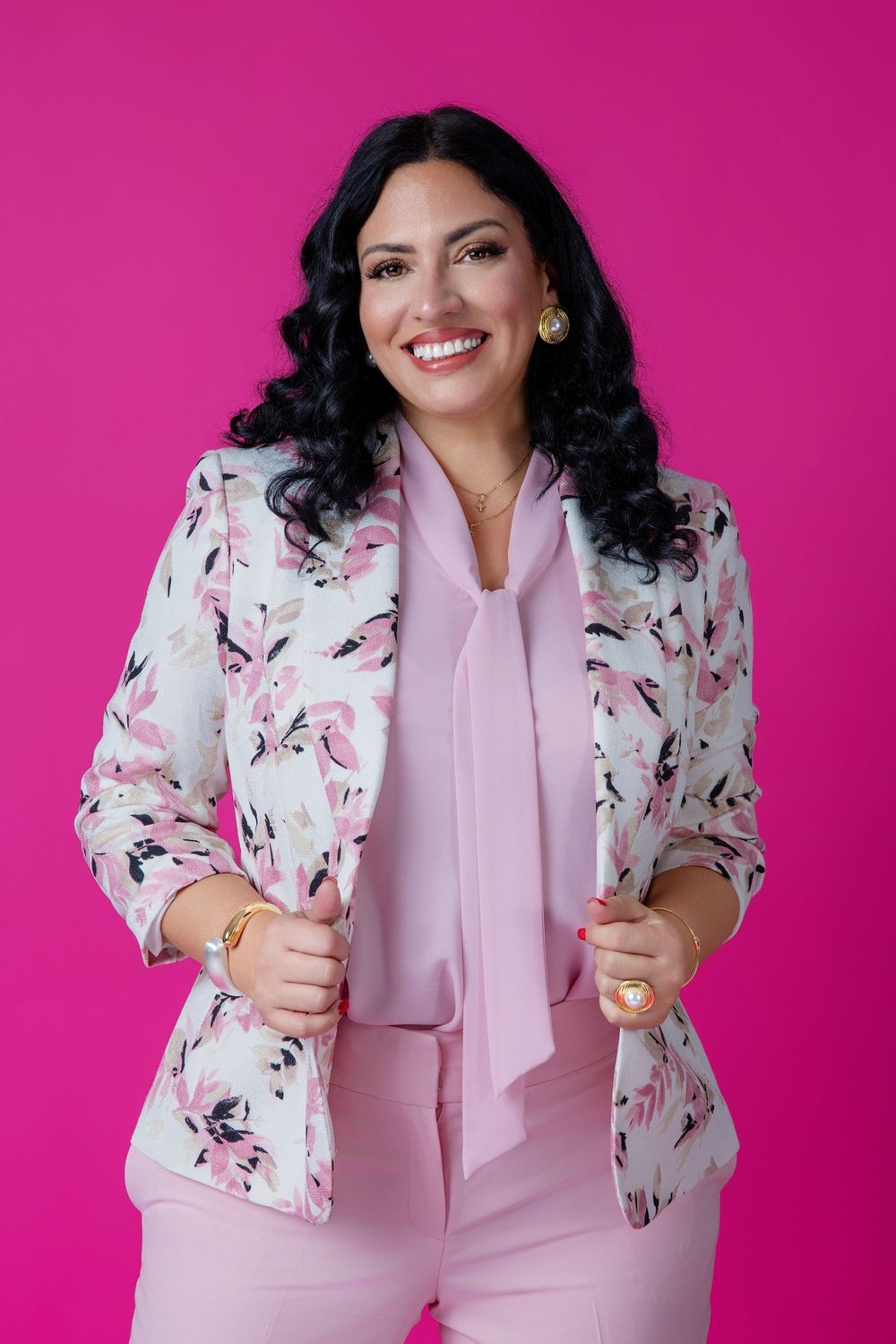 Smiling woman in pink floral blazer and blush outfit poses confidently against vibrant magenta background.