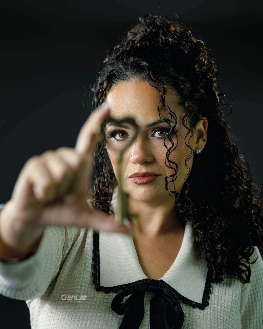 A woman with curly hair and artistic face paint poses confidently, extending her finger toward the camera in a dramatic portrait.