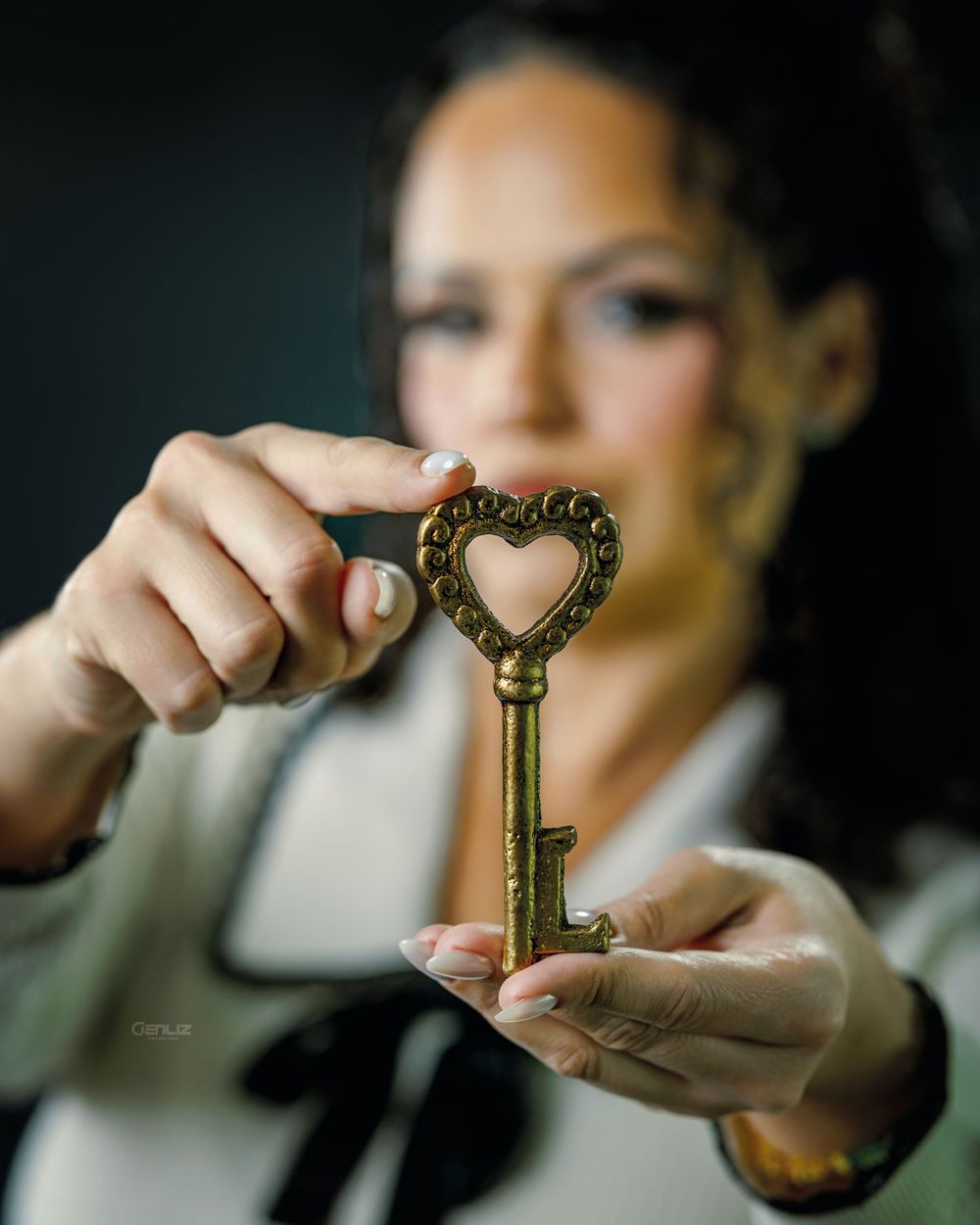 Woman holding an ornate brass skeleton key with heart-shaped bow in focus against blurred background.