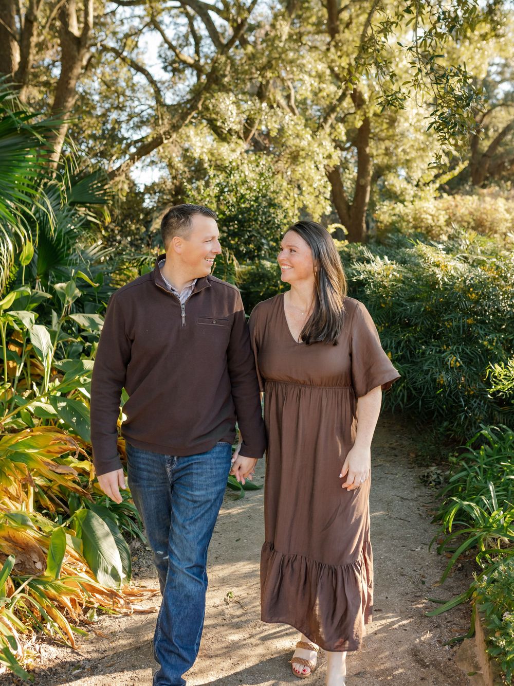 A couple strolls together on a garden path surrounded by lush tropical plants and trees.