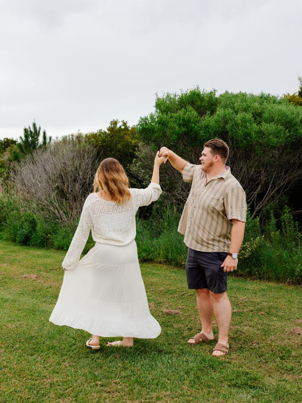 Two people dance playfully on grass, with one twirling in a white dress while the other leads.