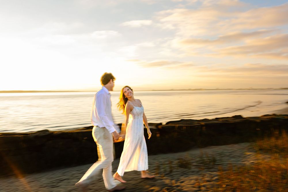 A couple walks hand in hand along the shoreline during sunset.