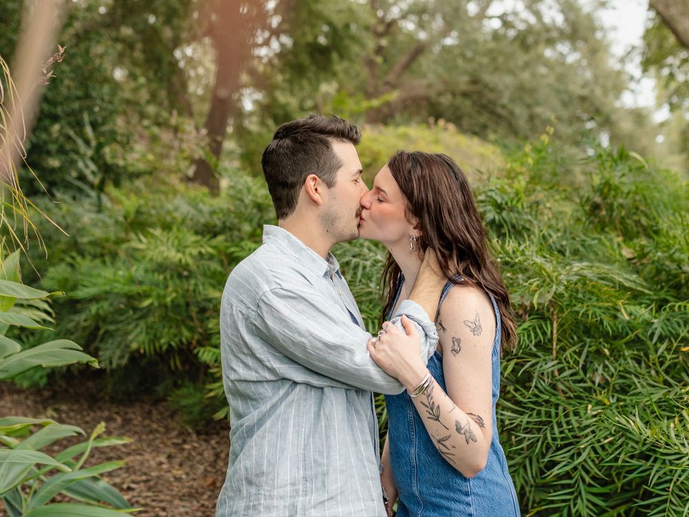 Romantic couple embracing in a lush garden setting with green foliage in background.