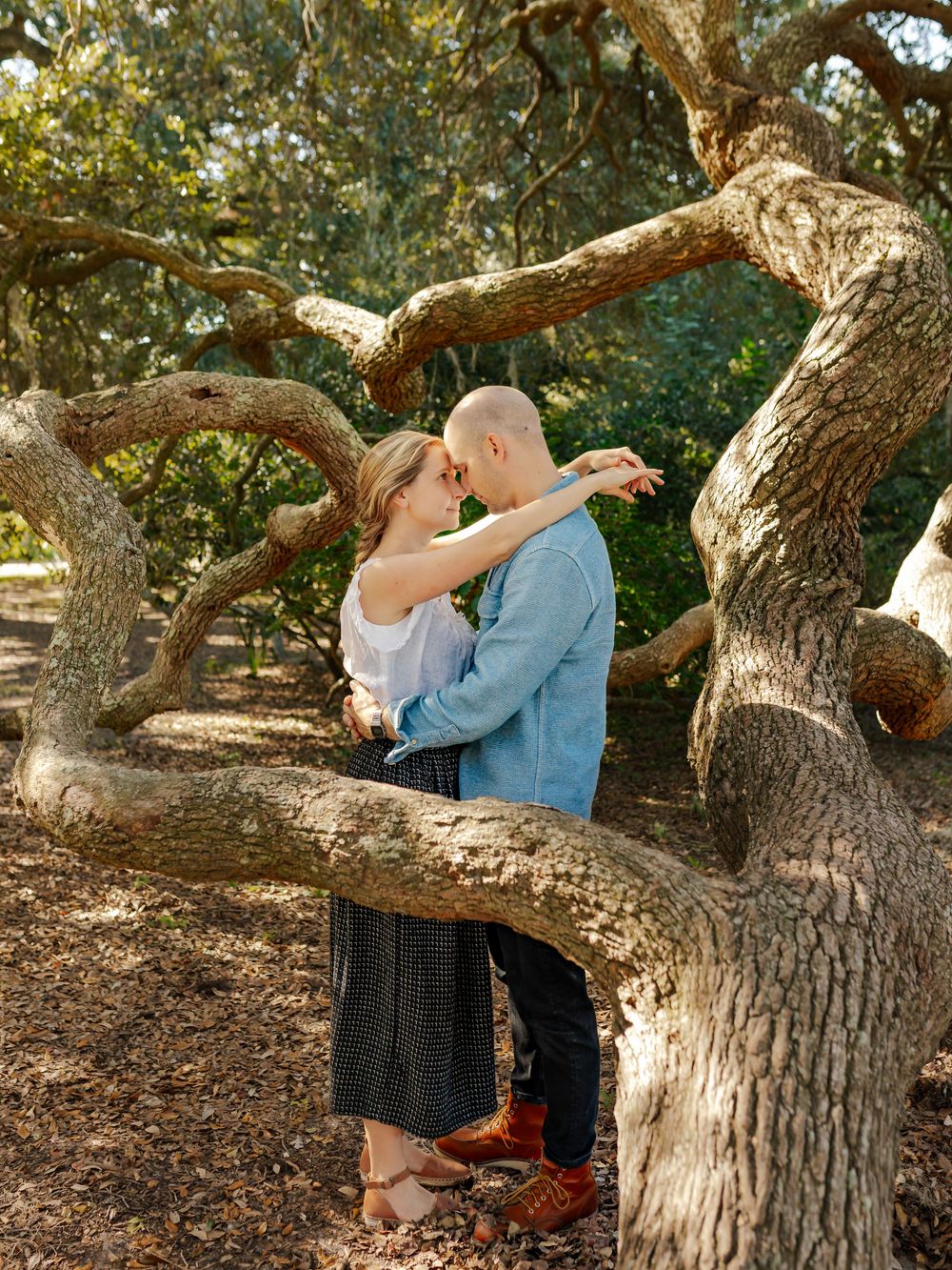 A couple shares an intimate moment beneath a sprawling oak tree with hanging moss.