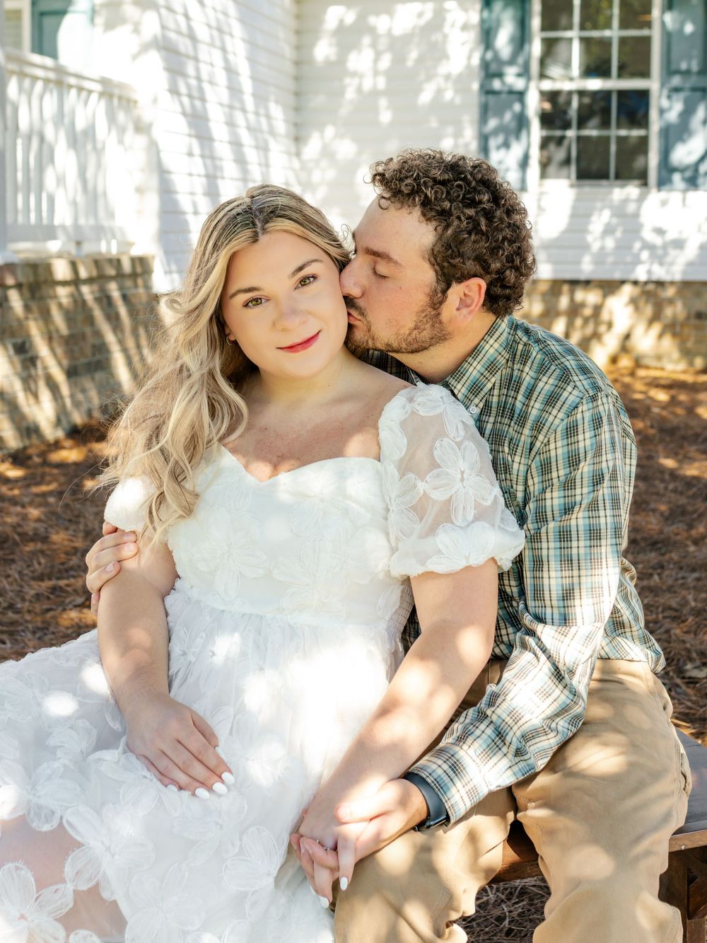 Sunlit portraits of a couple sharing affectionate moments against a white building.
