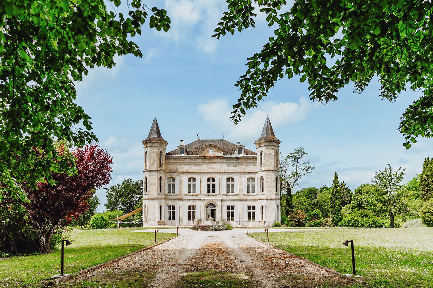 A panoramic view of a historic French chateau with manicured lawns and turrets set against a bright blue summer sky.