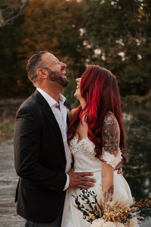 Laughing bride with red hair and groom embracing outdoors during autumn wedding portrait session.