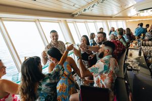 Wedding guests in tropical attire toasting drinks at a bar aboard a cruise ship reception.