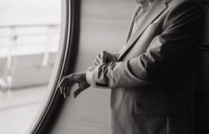 Black and white close-up of groom in suit adjusting cufflinks near large oval window.
