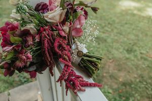 Lush bridal bouquet with deep red amaranthus, burgundy roses, and pink blooms resting on a white surface.