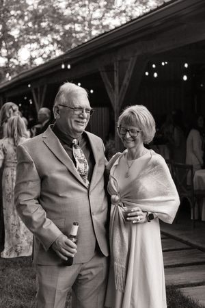 Elegant older couple smiling together outdoors at a wedding reception with string lights in the background.