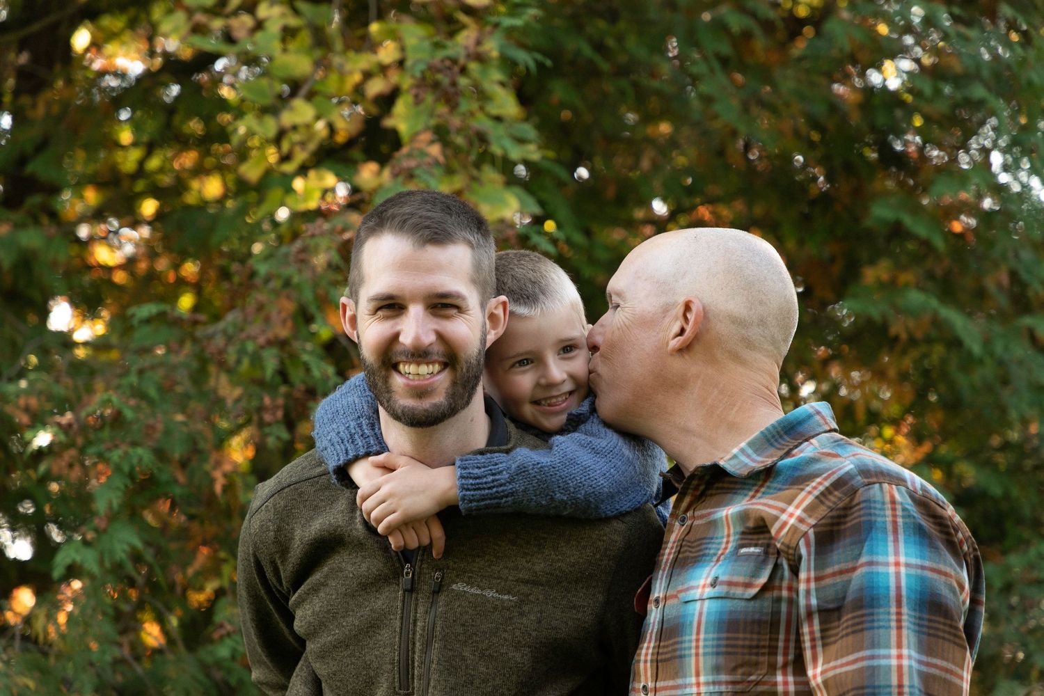 A father piggy backing his son. with a grandpa leaning over to kiss the grandson on the cheek