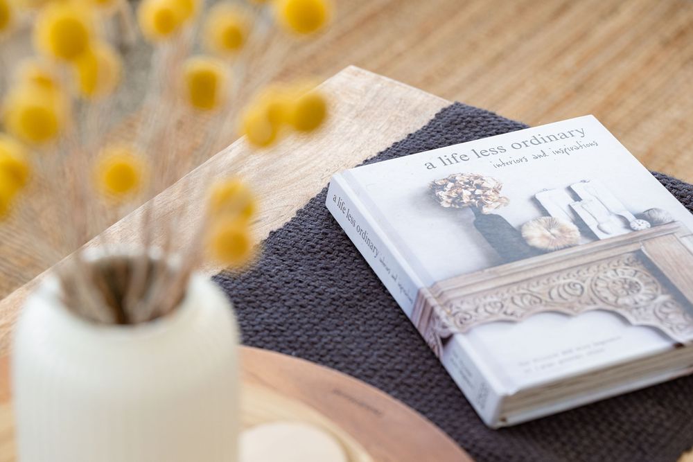 A book with decorative ribbon lies on a gray surface next to yellow flowers and a white candle.