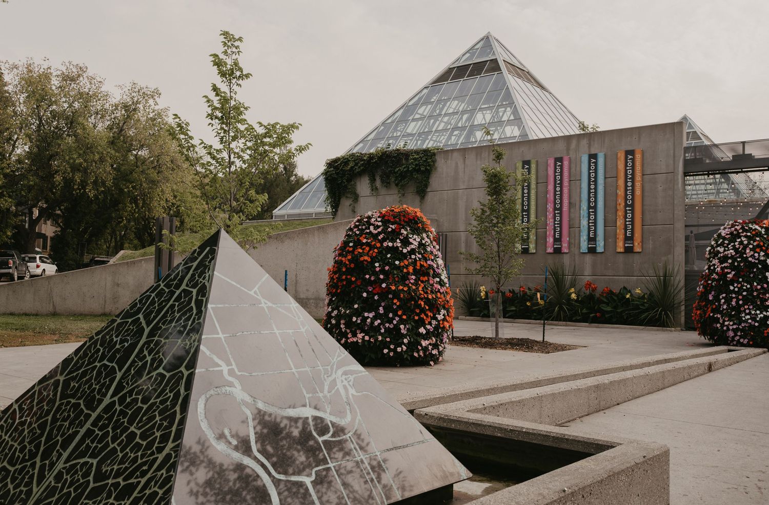 Modern glass pyramid structure with colorful illuminated panels and seasonal decorations in an outdoor garden setting.