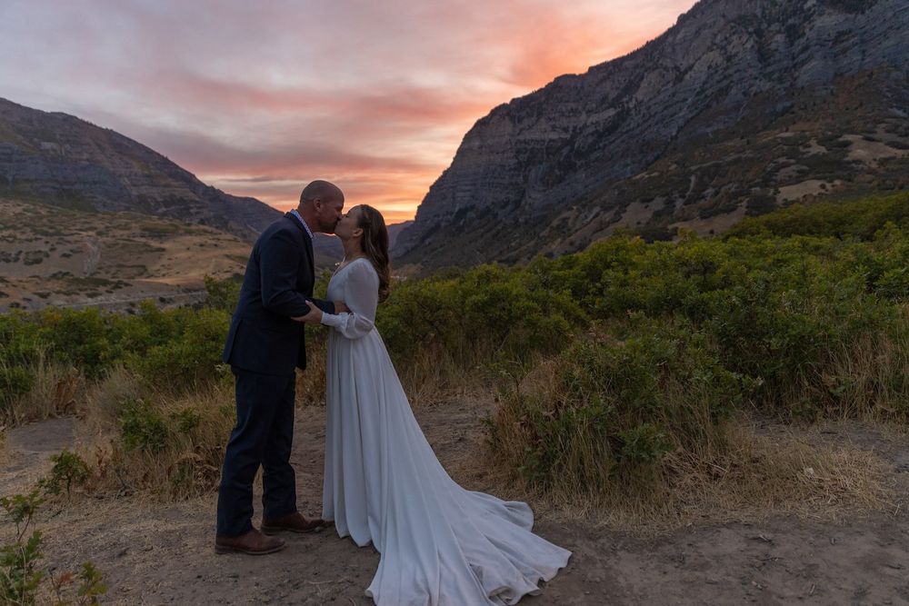 A scenic mountain elopement ceremony at sunset with dramatic rocky cliffs and pink sky.