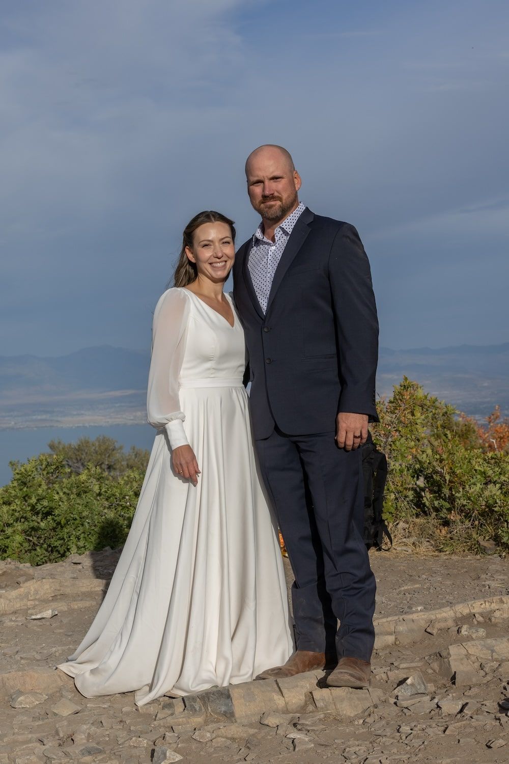 A wedding couple poses against a rocky landscape with mountains and blue sky in the background.