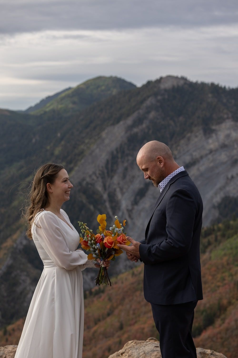 A couple exchanges vows and flowers during their intimate mountain elopement ceremony against a dramatic mountain backdrop.