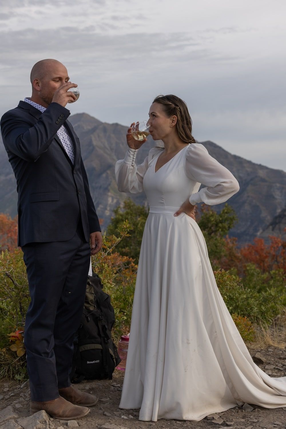 A couple shares playful moments in their wedding attire against a scenic mountain backdrop during autumn.