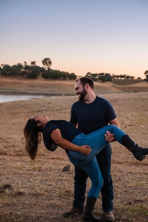 A couple dances playfully on the shoreline at sunset, creating a romantic silhouette against the golden sky. By lake hogans waters
