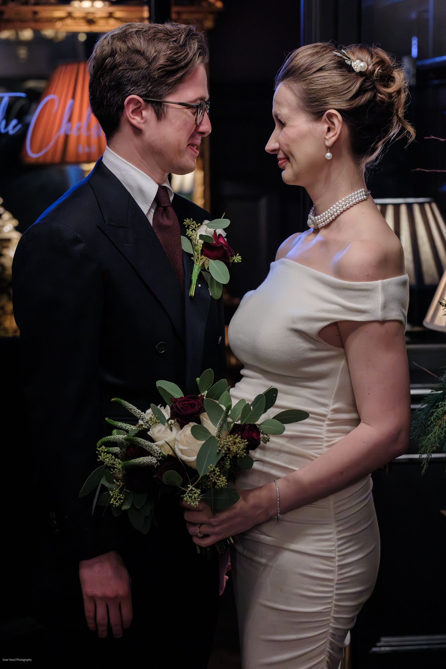 A couple in wedding attire share an intimate moment with the bride in a fitted cream dress holding white flowers.