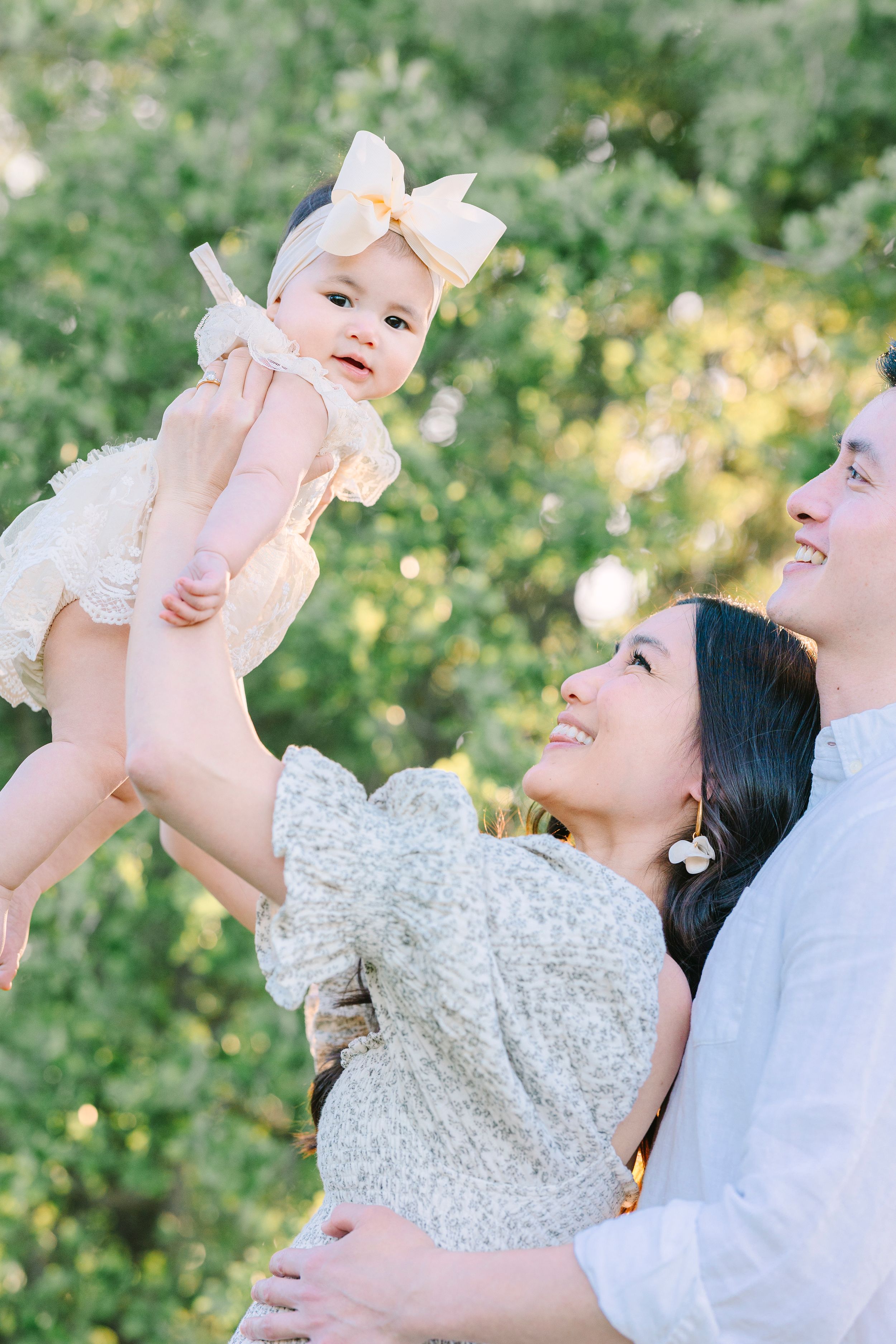A family plays and laughs together while holding their baby in an outdoor setting.