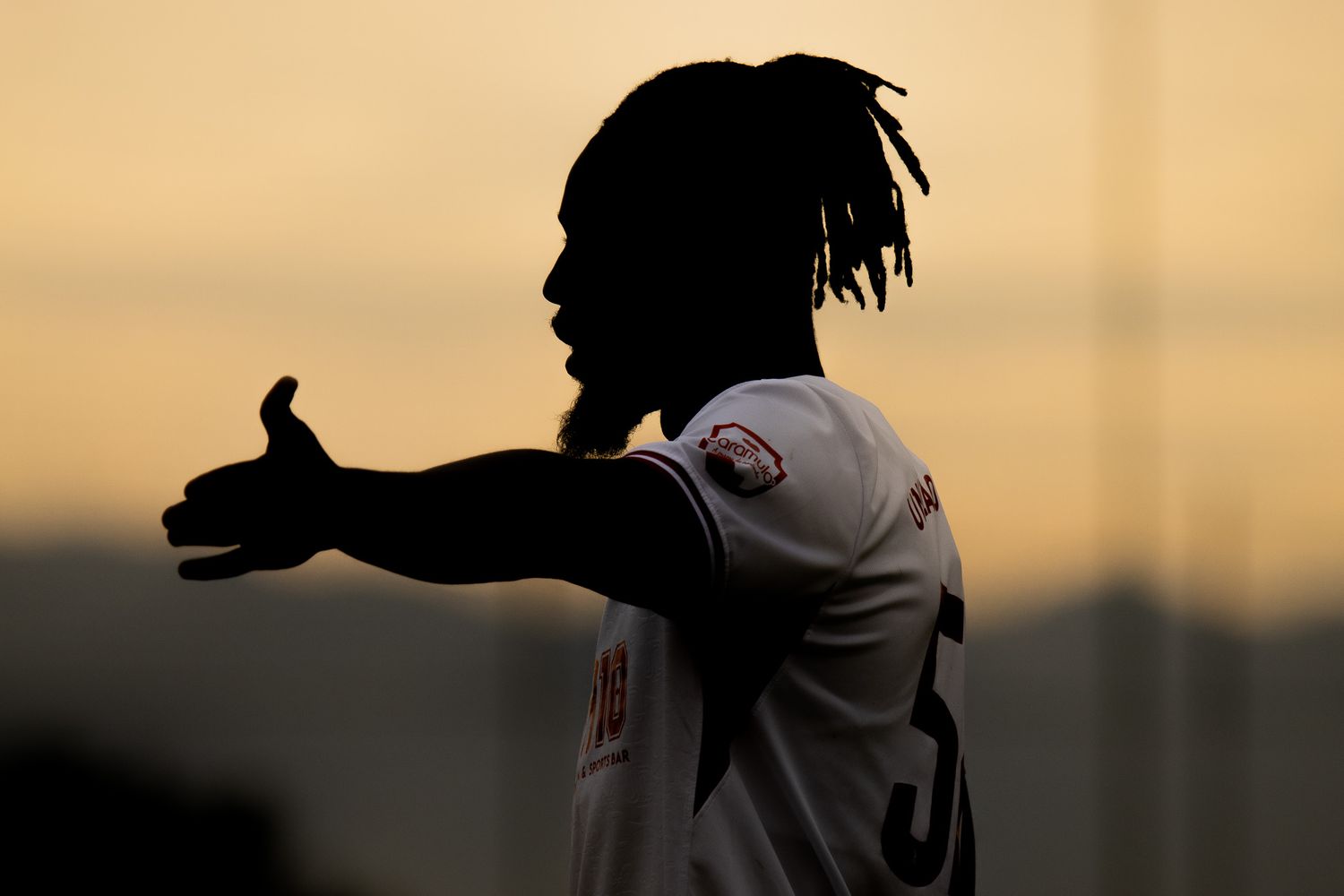 Silhouettes of soccer players against a warm sunset sky during a match.