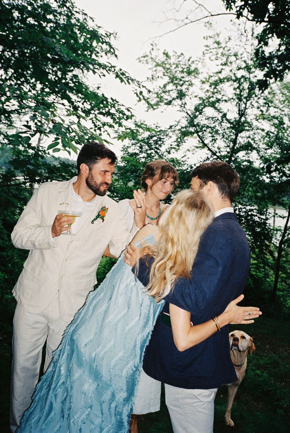 Candid scene of the groom showing off his new wedding ring to his brother, holding his girlfriend and his wife smiles while the dog watches.