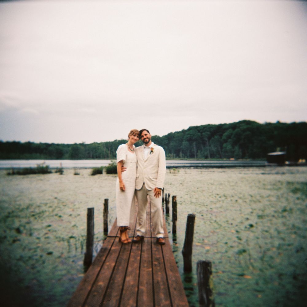 Square crop of couple standing on a dock in a sea of lily pads on a lake in Rhinebeck, NY. Just married & posing together under overcast sky