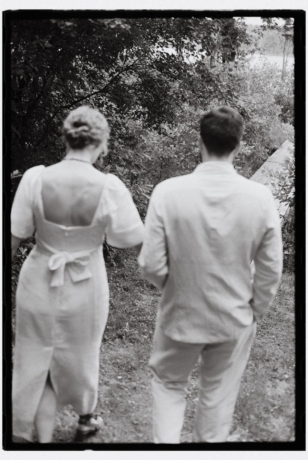 Black and white photo of the bride and groom walking together towards the dock for intimate portraits after their outdoor ceremony in NY.