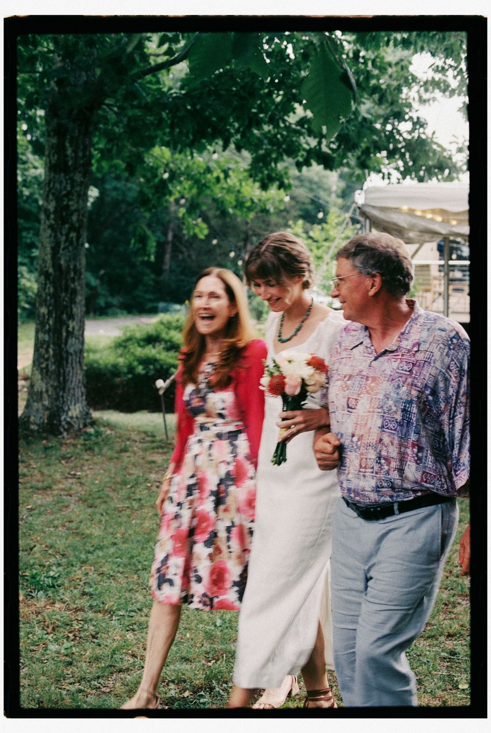 Documentary photo of parents of the bride walking her down the aisle while the mother joyfully laughs and the father smiles in upstate NY.