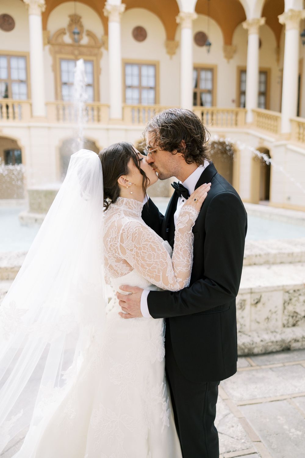 Romantic wedding couple embracing in front of ornate columns and arches of a historic building.