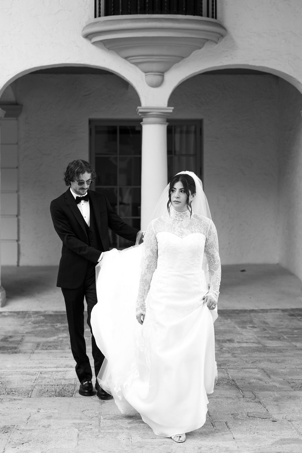 Black and white wedding photos showing playful moments between newlyweds under arched walkways.