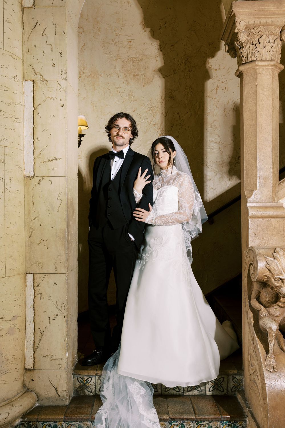 Elegant wedding couple posing in a stone archway with ornate architectural details.