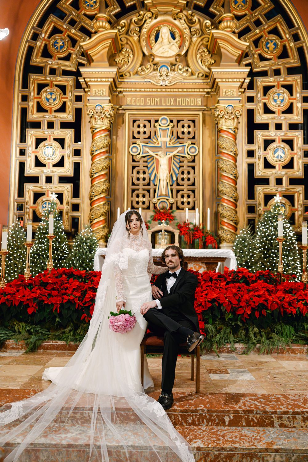 Wedding portrait in front of ornate architecture with red poinsettias and Christmas decorations.