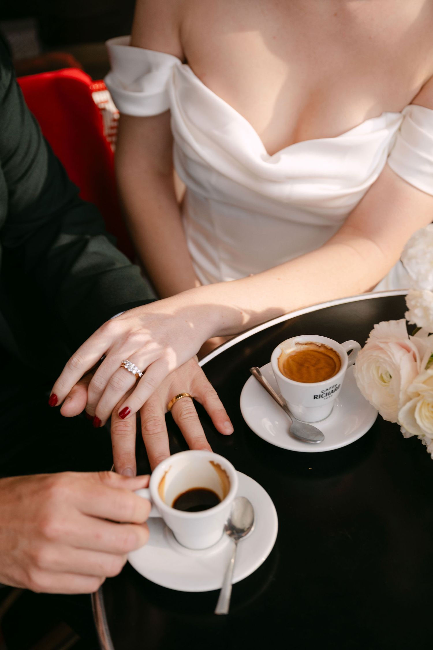 Couple sharing espresso drinks at a romantic moment with white roses and wedding rings visible.