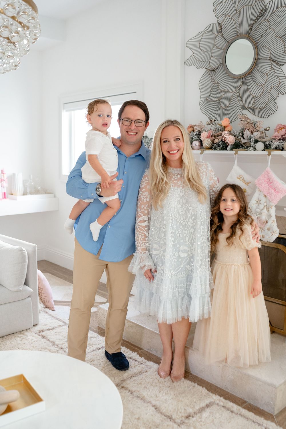 Family wearing coordinated white and beige outfits posing together in a bright modern living room.