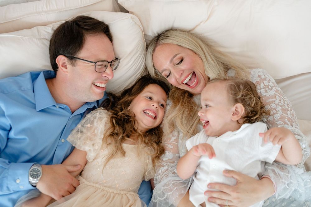 A joyful family shares intimate moments while lying together on white bedding.